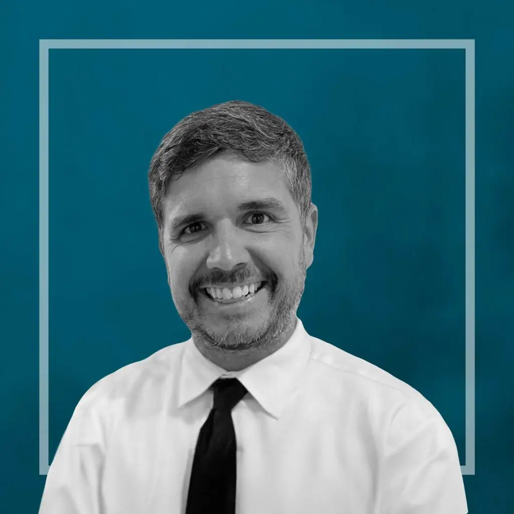 Here's an alt tag for the image: Smiling man in a white shirt and tie.